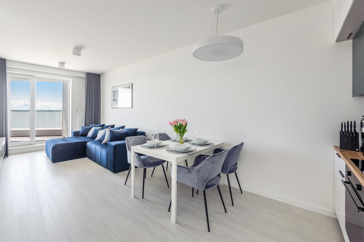 Un salon moderne comprenant un coin repas, un ensemble de canapés et une vue sur la mer grâce à de grandes fenêtres.