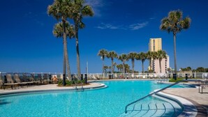 Una piscina azul cristalina rodeada de palmeras y un rascacielos al fondo.