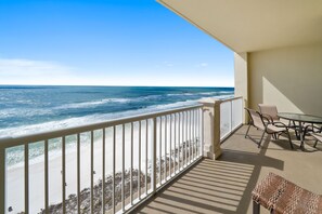 Ein Balkon mit Blick auf das Meer, ein Tisch mit Stühlen und eine Korbsitzbank.