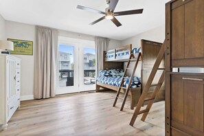 A room with a bunk bed, a ceiling fan, a wooden wardrobe, and a view of the outside. - Water's Edge by Brunswick Vacation Rentals: Home w/ Pool & Elevator, Near Beach (Ocean Isle Beach)