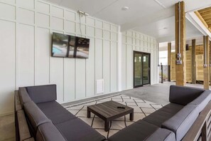 A modern lobby with a sofa, a coffee table, and a TV mounted on the wall. - Water's Edge by Brunswick Vacation Rentals: Home w/ Pool & Elevator, Near Beach (Ocean Isle Beach)