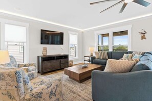 Una sala de estar con sofá, sillón, mesa de centro, televisor y ventilador de techo.