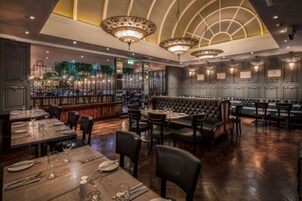 Un restaurante con techo alto, candelabros y una zona de bar. Las mesas están dispuestas con vajilla.