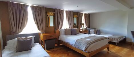 Een hotelkamer met drie bedden, houten vloeren en grote ramen met gordijnen.