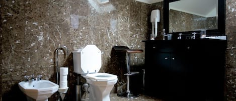 Un baño con pared de mármol, un bidé, un inodoro, un lavabo y un espejo.