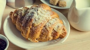A croissant on a plate with a cup of coffee and a sugar bowl in the background.
