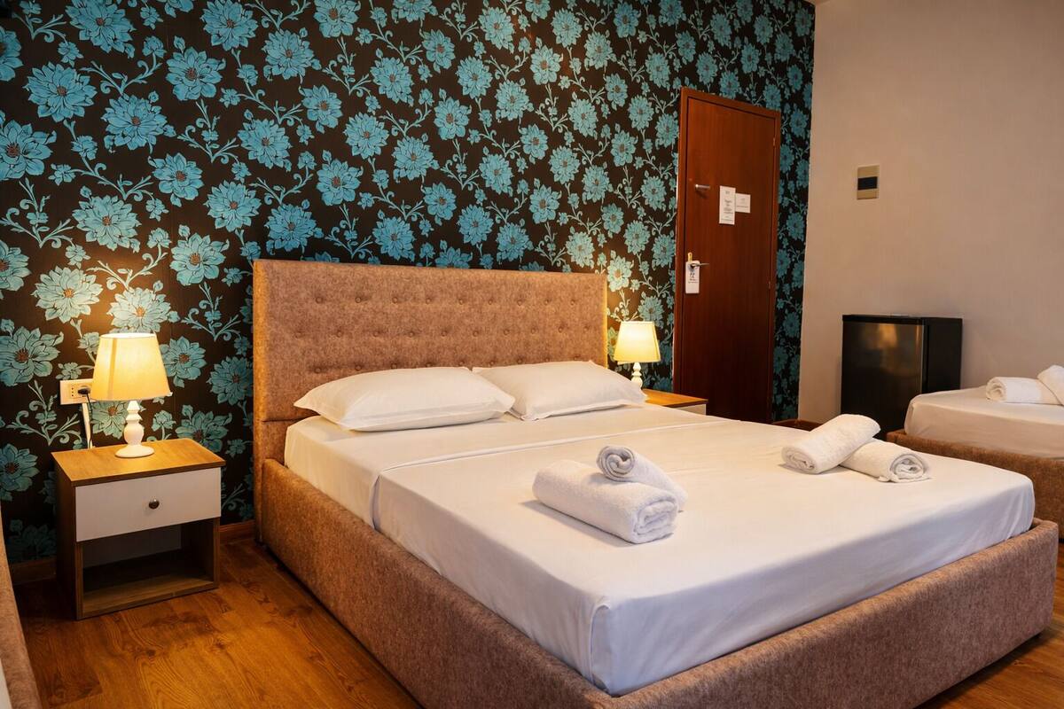 A hotel room with a large bed, two bedside tables with lamps, a wardrobe, and a TV.
