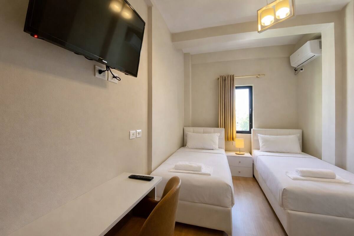 A hotel room with a TV, two beds, a desk, and a chair.
