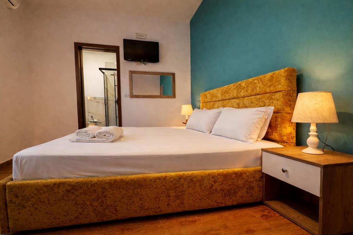 A hotel room with a bed, bedside table, lamp, TV, and a mirror.