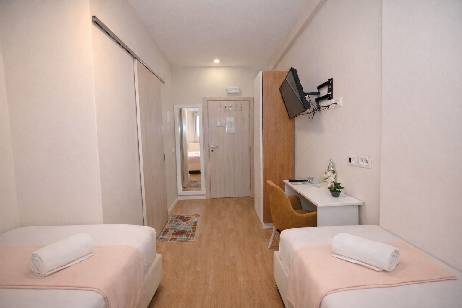 A hotel room with two beds, a desk, a TV, and a bathroom visible through an open door.