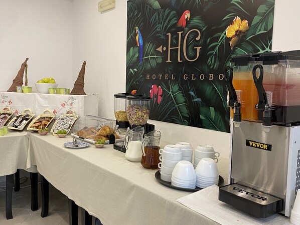 Un bufé de desayuno con diversos alimentos, una máquina de café y una pared con motivos tropicales.