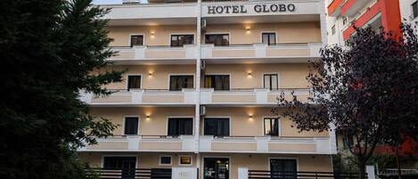 Um hotel de vários andares chamado HOTEL GLOBO, com fachada moderna, varandas e um estacionamento na frente.