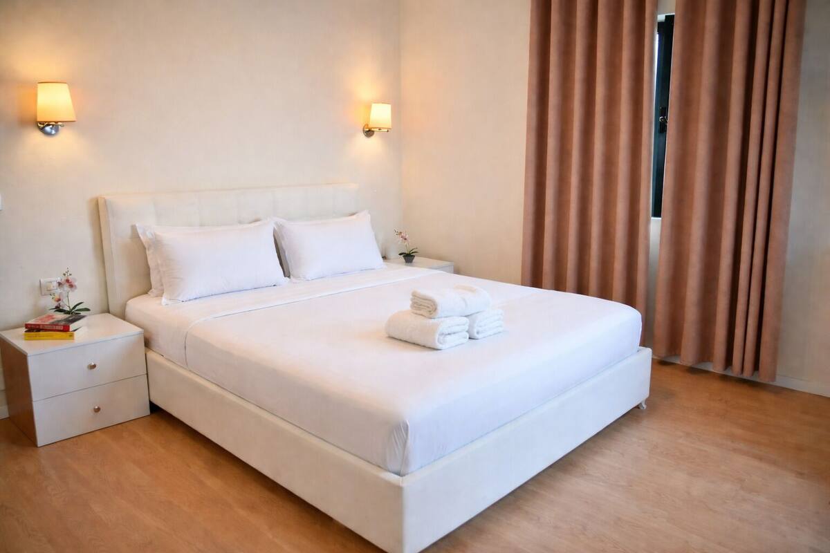 A neatly made bed with white linens, two bedside tables, and a nightstand with a lamp.
