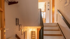 Un escalier en bois avec une rampe, un radiateur sur le côté gauche et des tableaux encadrés accrochés aux murs.