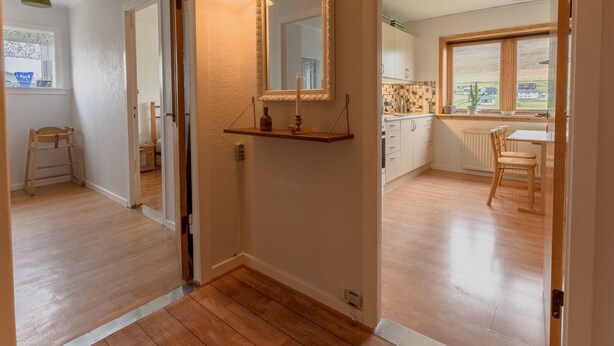 Un couloir mène à une cuisine dotée d’un plancher en bois, d’un miroir et d’une fenêtre donnant sur des maisons.