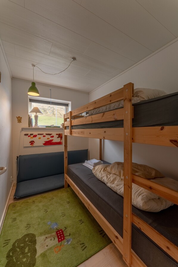 A bunk bed room with a window, a desk with a lamp, and a green rug.