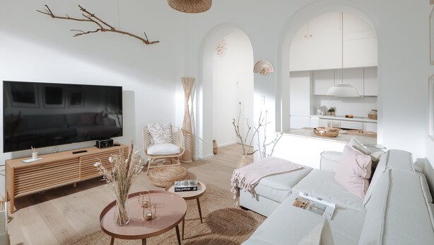 Una sala de estar moderna con un televisor de pantalla plana grande, un sofá blanco, un sillón de mimbre y una mesa de centro.