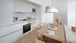 Una cocina moderna con armarios blancos, horno empotrado y comedor con mesa y sillas de madera.
