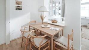 Un comedor con una mesa de madera y cuatro sillas, una lámpara blanca y un jarrón con plantas secas.