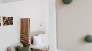 A minimalist living room with a white sofa, a wooden panel, and a small table. - // V I L L A F R E S E N A // Bude 3 (Norderney)