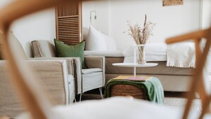 A cozy living room with a sofa, a side table with a vase, and a chair. - // V I L L A F R E S E N A // Bude 3 (Norderney)