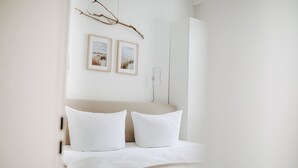 A minimalist bedroom with a bed, two pillows, a branch decoration, and two framed pictures on the wall. - // V I L L A F R E S E N A // Bude 6 (Norderney)