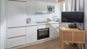 A compact kitchen with a microwave, oven, and coffee maker. A television is mounted on a wooden stand. - // V I L L A F R E S E N A // Bude 6 (Norderney)