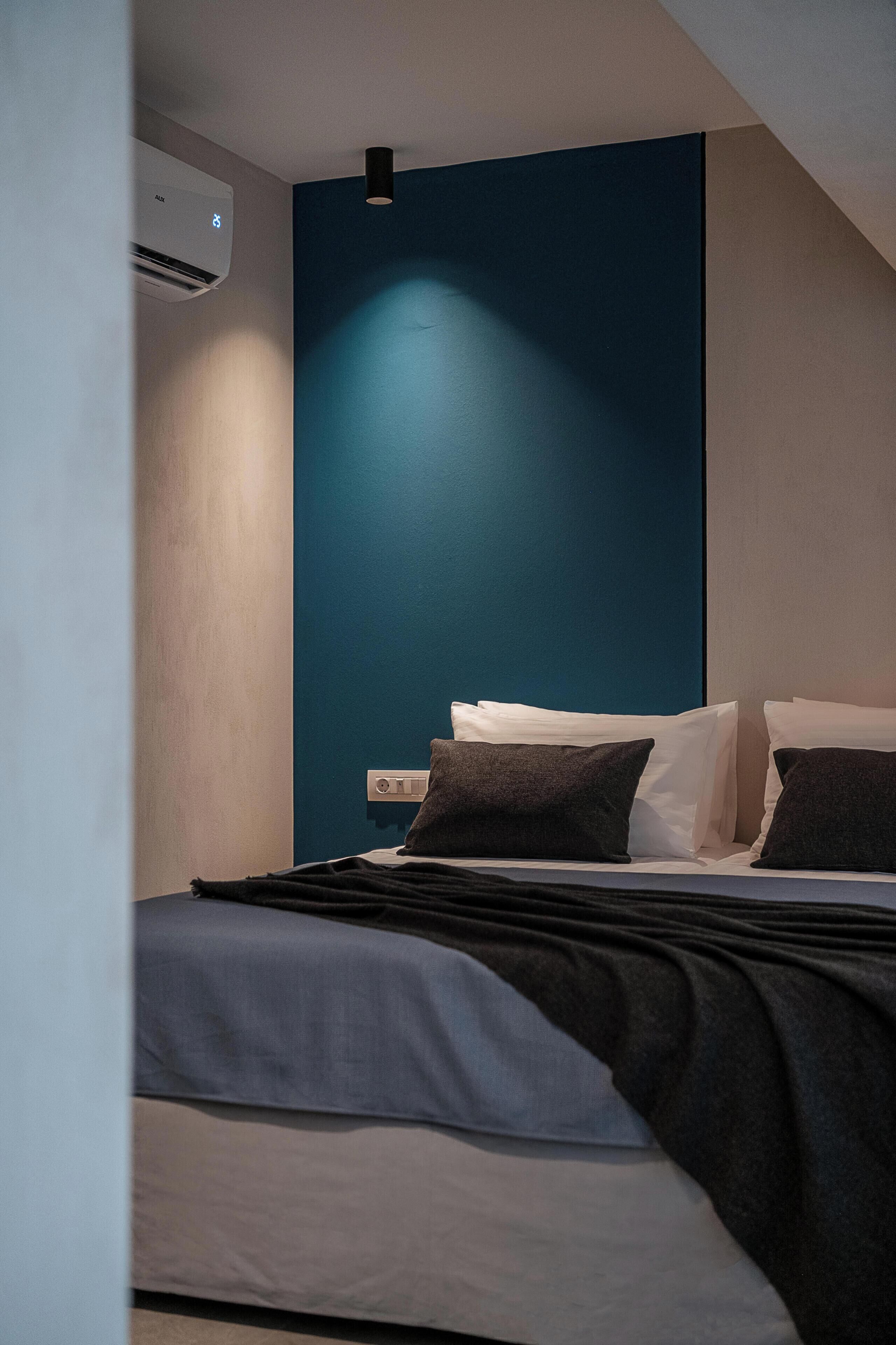 A modern hotel room with a bed, a wall-mounted air conditioner, and a blue accent wall.