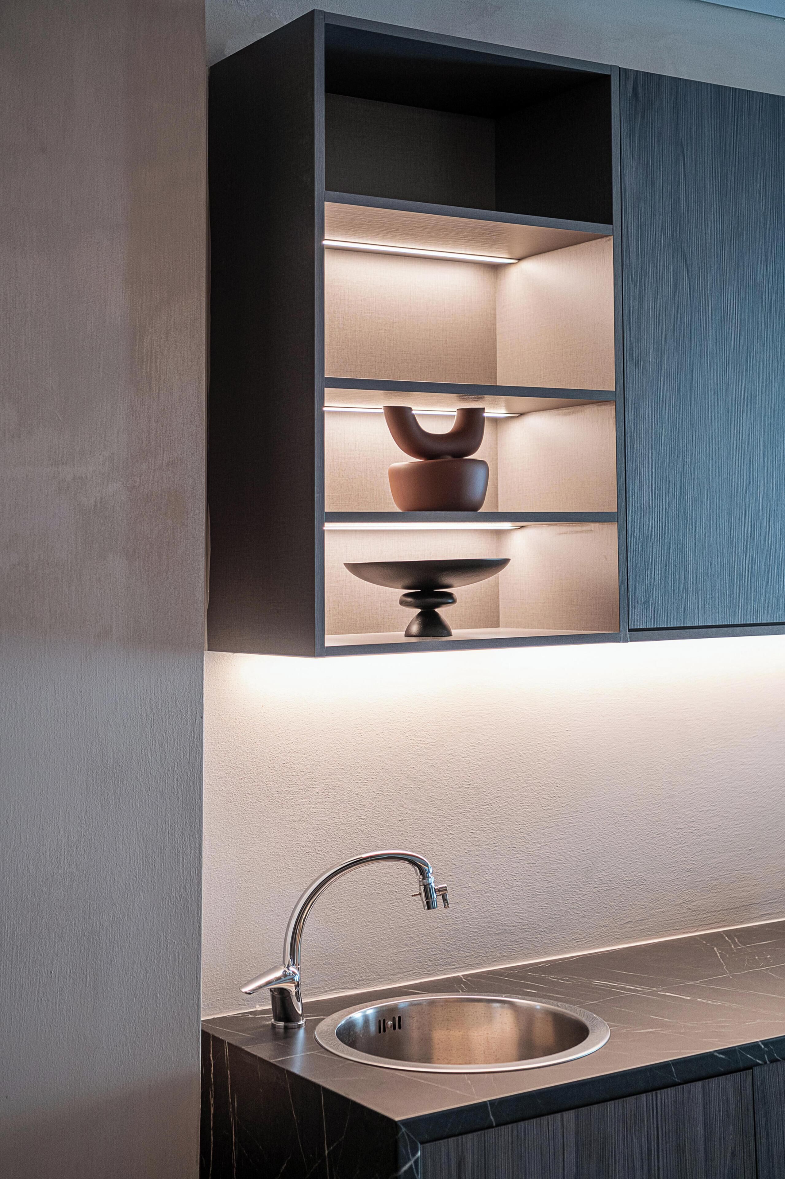 A modern kitchen with a built-in shelf unit, a stainless steel sink, and a marble countertop.