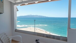 A balcony with white chairs, a small table, and a view of the beach and ocean. - Hotel Emblem (Sarandë)