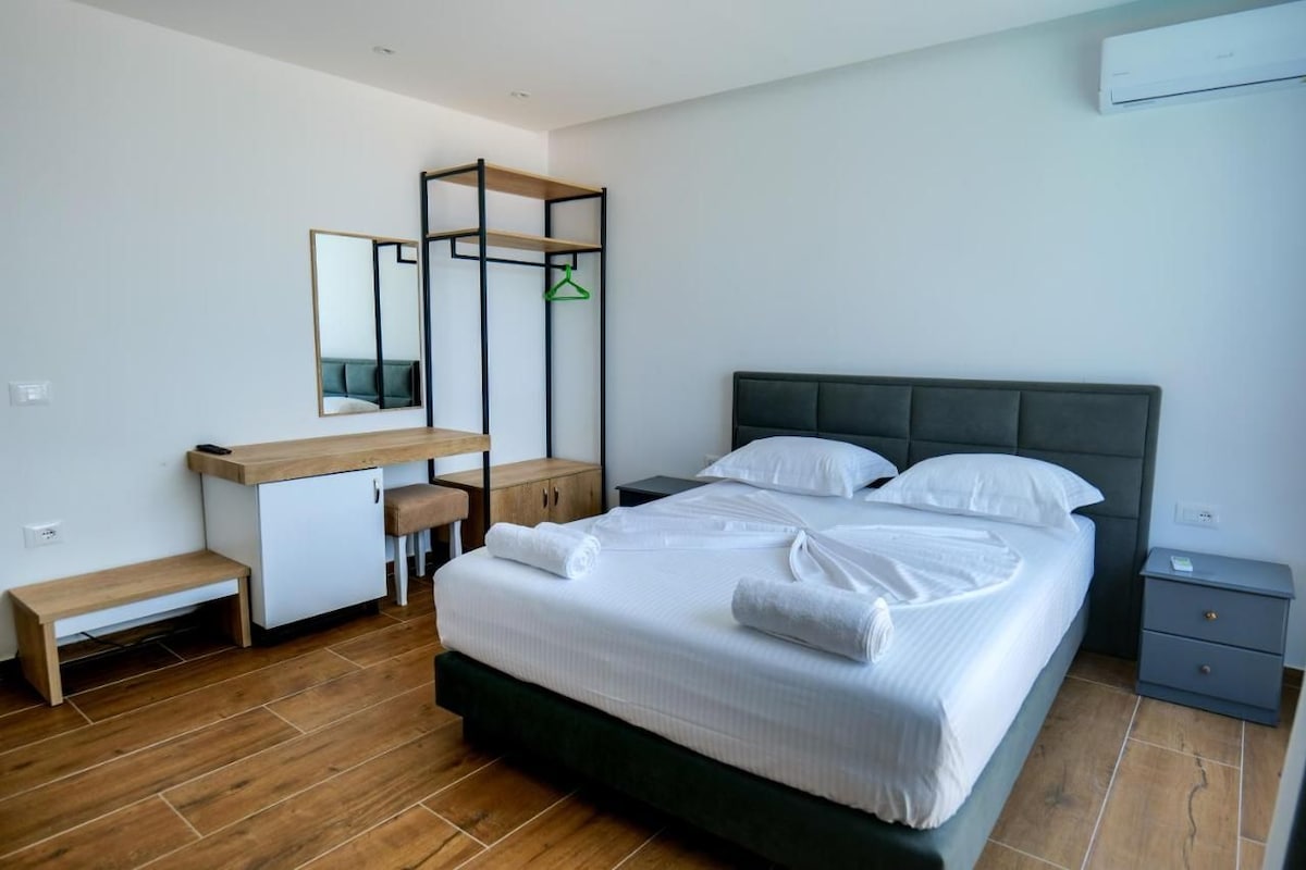 Een slaapkamer met een bed, een bureau, een stoel, een spiegel en een kledingrek.