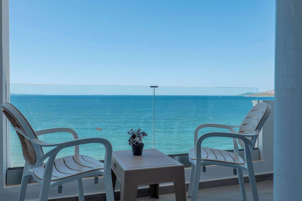 A balcony with two white chairs and a small table, overlooking a clear blue sea.