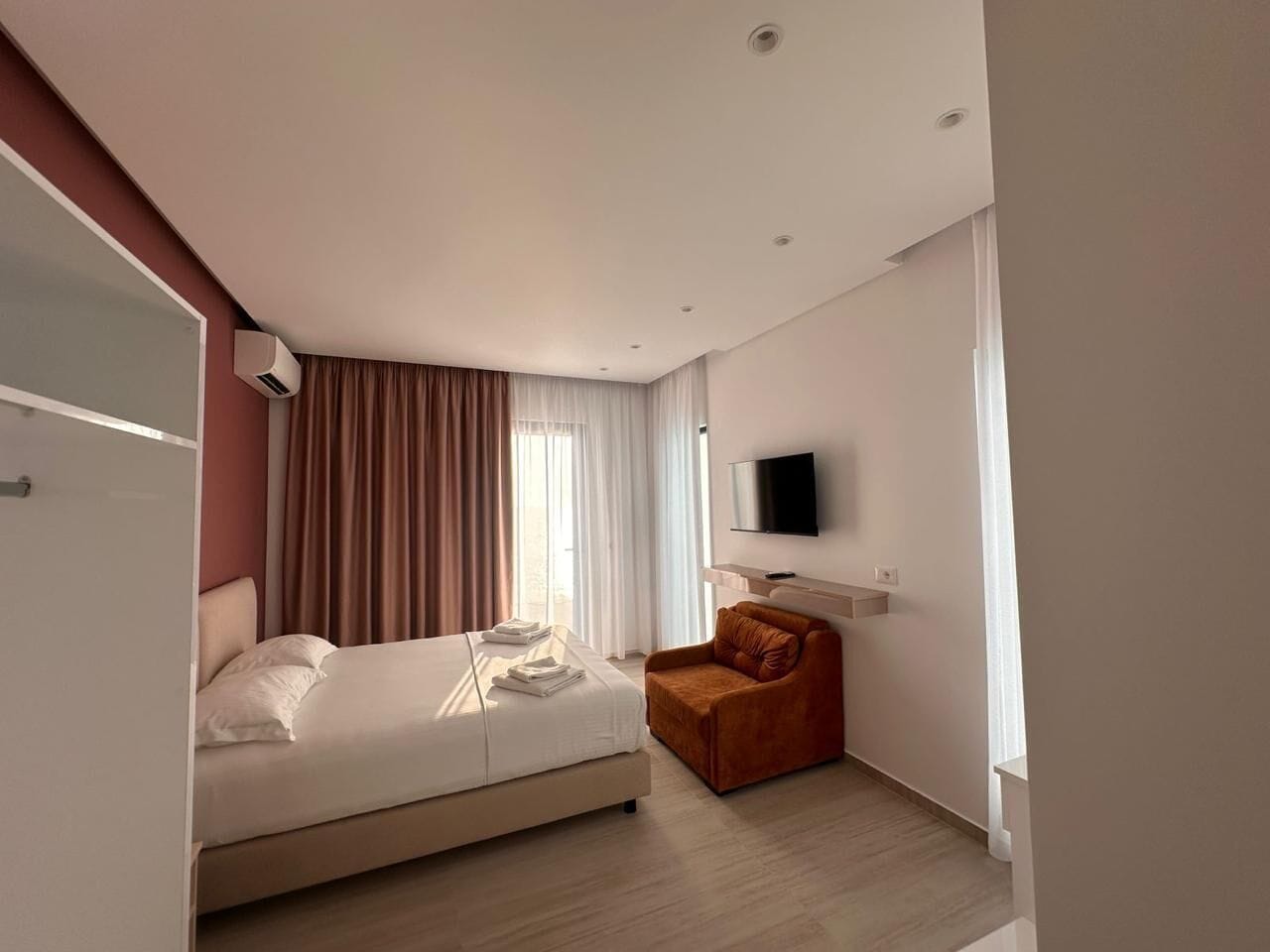A modern hotel room with a bed, a chair, a TV, and a window with curtains.