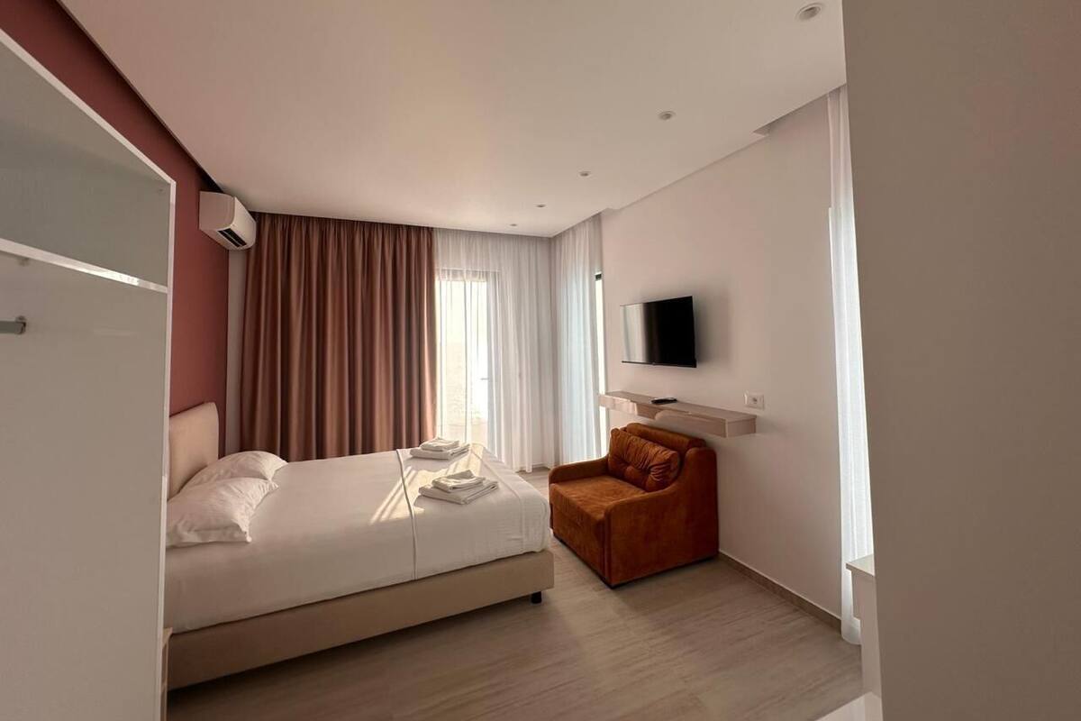 A modern hotel room with a bed, a chair, a TV, and a window with curtains.