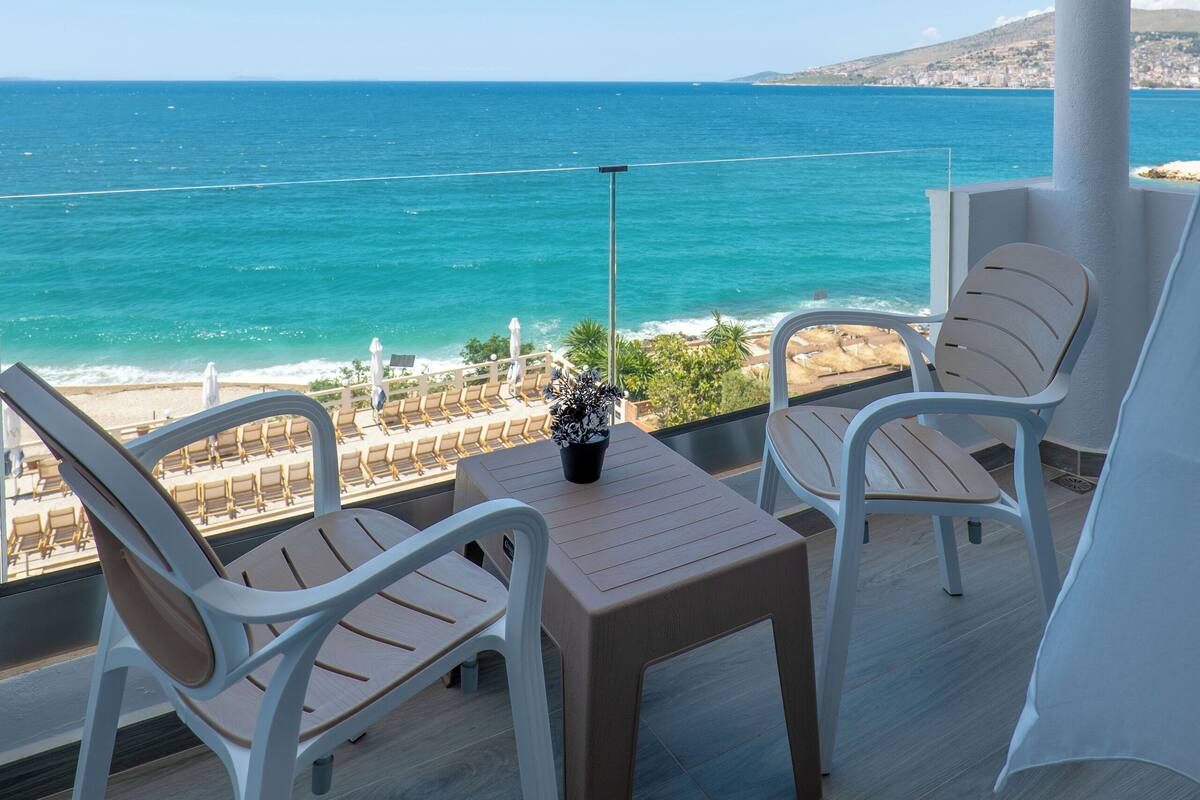 A balcony with a view of the sea, two chairs, a table, and a potted plant.