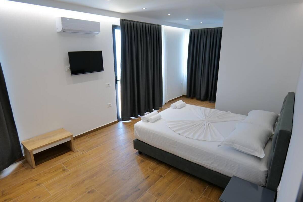 A modern hotel room with a bed, a TV, a small wooden bench, and a window with curtains.