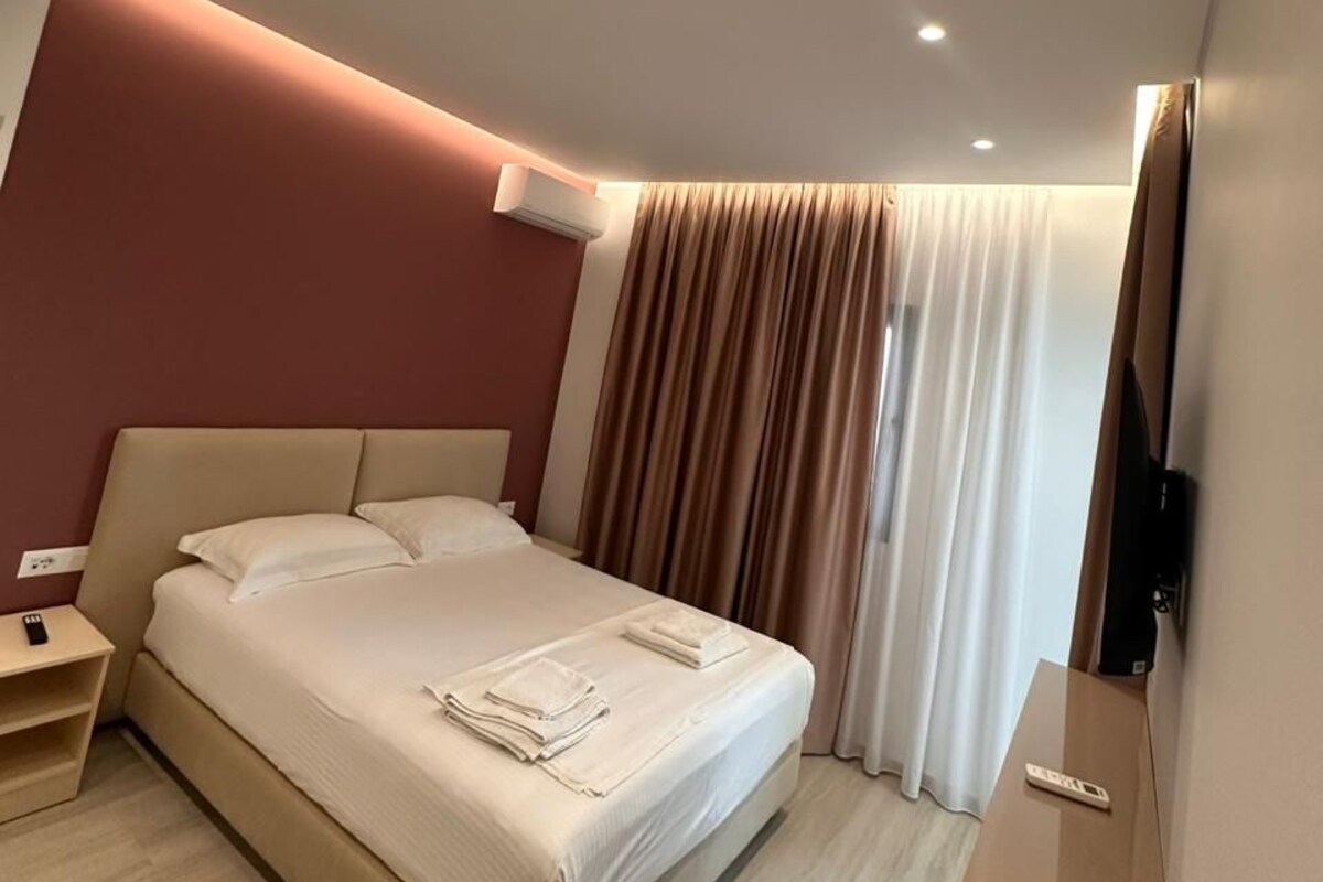 Una habitación de hotel moderna con una cama grande, una mesita de noche, un equipo de aire acondicionado y un televisor de pantalla plana montado en la pared.