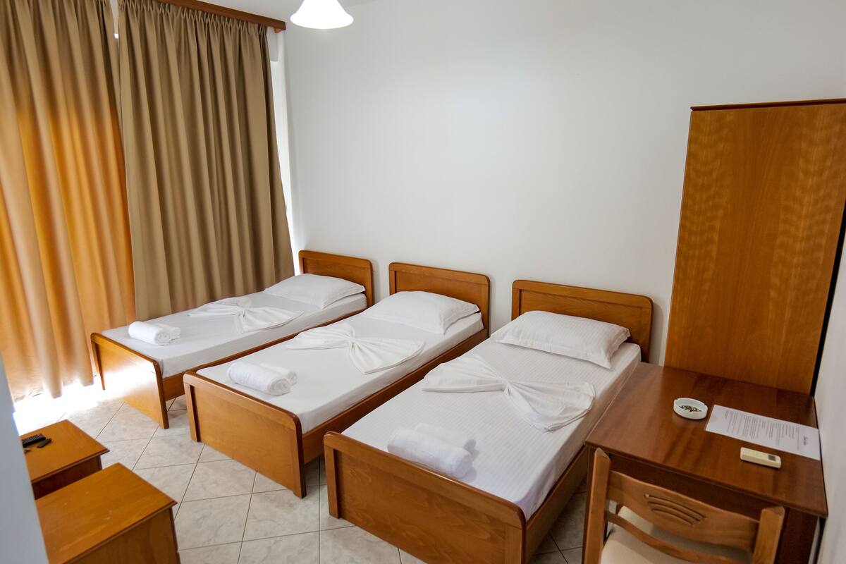 A hotel room with two single beds, a wooden desk, a chair, a bedside table, and a large mirror.