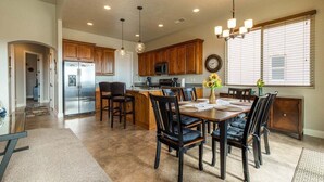 A modern kitchen with wooden cabinets, a stainless steel refrigerator, and a dining area with a table and chairs. - Desert Escape: Sand Dunes + Golf + Resort Access (Hurricane)