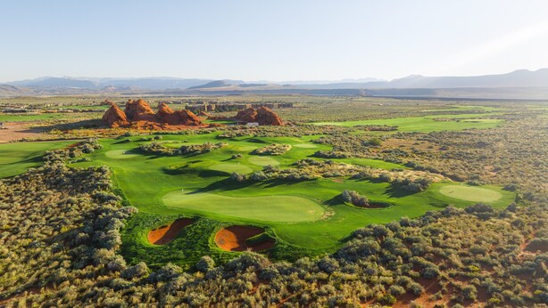 A golf course with multiple greens and bunkers, surrounded by desert vegetation and red rock formations. - Desert Escape: Sand Dunes + Golf + Resort Access (Hurricane)