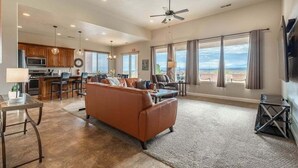 A spacious living room with a large sofa, a dining area with a kitchen in the background, and large windows offering a view. - Desert Escape: Sand Dunes + Golf + Resort Access (Hurricane)