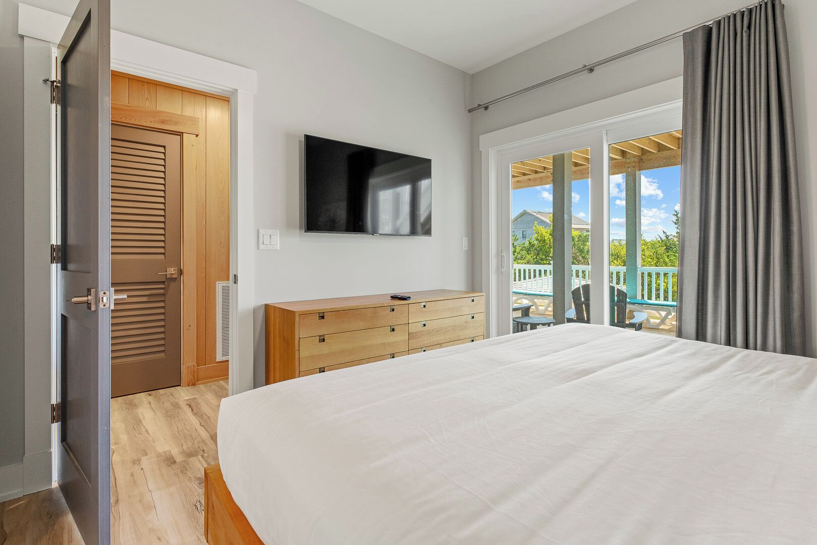 A bedroom with a large bed, wooden dresser, and a TV on the wall.