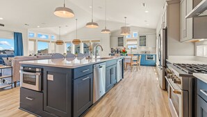 Cozinha moderna com ilha central, eletrodomésticos de aço inoxidável e iluminação pendente.
