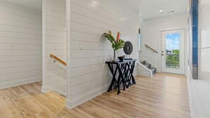 Interior moderno com paredes brancas em painel, assoalho de madeira, uma escada e uma pequena mesa com objetos decorativos.