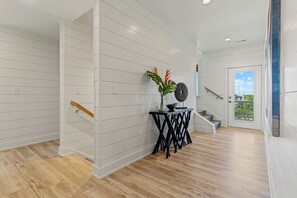 Un intérieur moderne avec des murs recouverts de panneaux blancs, un plancher en bois, un escalier et une petite table agrémentée d’objets décoratifs.