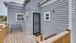 Una casa con una terraza de madera, un banco de metal negro y una puerta gris.