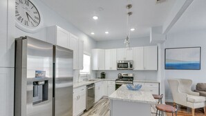 Una cocina moderna con electrodomésticos de acero inoxidable, armarios blancos y una barra con taburetes.