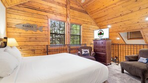 Una cabaña con interior de madera, una cama, un aparador, una silla y un televisor.