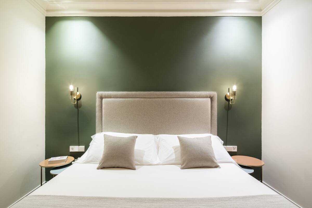 Una habitación de hotel con una cama grande, dos mesitas de noche e iluminación en la pared.