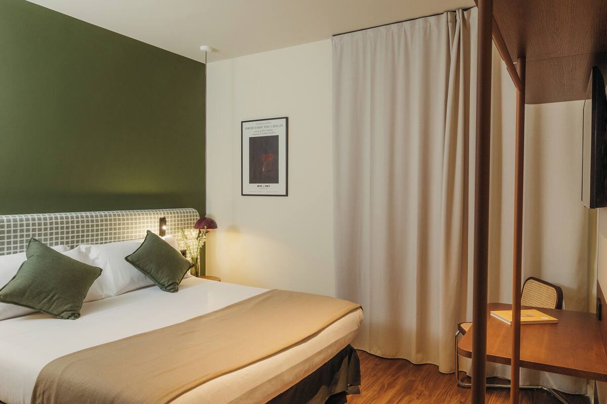 Una habitación de hotel con cama, escritorio y un cuadro en la pared.